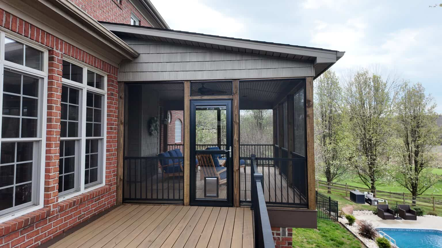 Screened porch with dark frames and a wood-plank ceiling joined to a composite deck